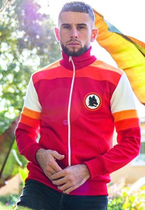 Rode ritsjack met contrasterende oranje en witte strepen op de mouwen. Voorzien van een rond logo op de borst. Gekocht met donkere spijkerbroeken.