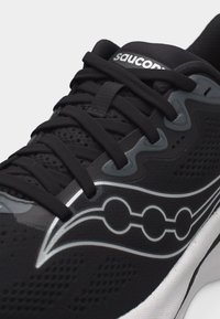Μαύρο αθλητικό παπούτσι Saucony με αεριζόμενο δίχτυ, μαύρα κορδόνια, ασημένιο λογότυπο στο πλάι και λευκή σόλα ορατή στο κάτω μέρος.