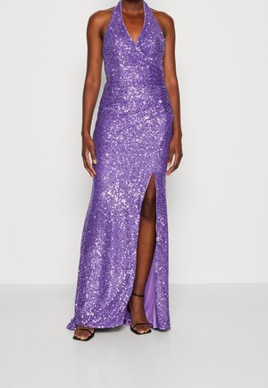 Lilla halterneck-kjole med pailletter, tætsiddende design, høj slids på låret og draperet tekstur, båret med sorte sandaletter med stropper.