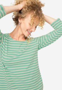 Maglietta a maniche lunghe a righe verdi e bianche con scollatura rotonda e vestibilità rilassata, realizzata in un tessuto morbido che cade delicatamente.