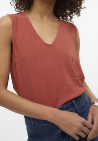 Haut sans manches de couleur rouille avec un décolleté en V, présentant un tissu texturé et une coupe décontractée, associé à un jean en denim taille haute.