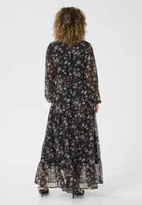 Maxime dress in mustassa läpinäkyvä kangas, jossa on vaaleanpunaisia kukkakuoseja, pitkät hihat, kerrokselliset röyhelöt helmassa ja muodikas vyötärö.