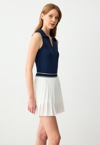 Marineblauwe mouwloze poloshirt met een kraag, gecombineerd met een geplooide witte rok met een zwart-wit gestreepte tailleband.
