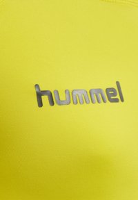 Heldere gele sportshirt met een gestructureerde stof en een glanzend, zilveren "hummel" logo in het midden.