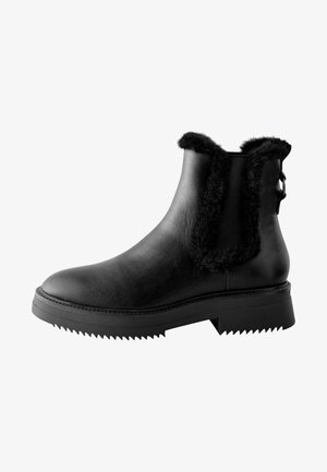 Bottes noires à la cheville avec un extérieur en cuir texturé, des accents de fourrure sur les côtés et une semelle en caoutchouc crantée pour plus d'adhérence. Présentent un détail de boucle.