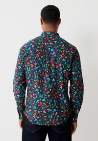 Camicia a maniche lunghe in tessuto blu navy scuro con una stampa colorata a tema invernale, che include alberi, regali e fiocchi di neve. Colletto standard.