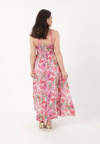 Maxikleid mit floralem Muster in Pink und Grün, gerafftem Oberteil, dünnen Trägern und fließendem Stoff. Getragen mit beigen High Heels.