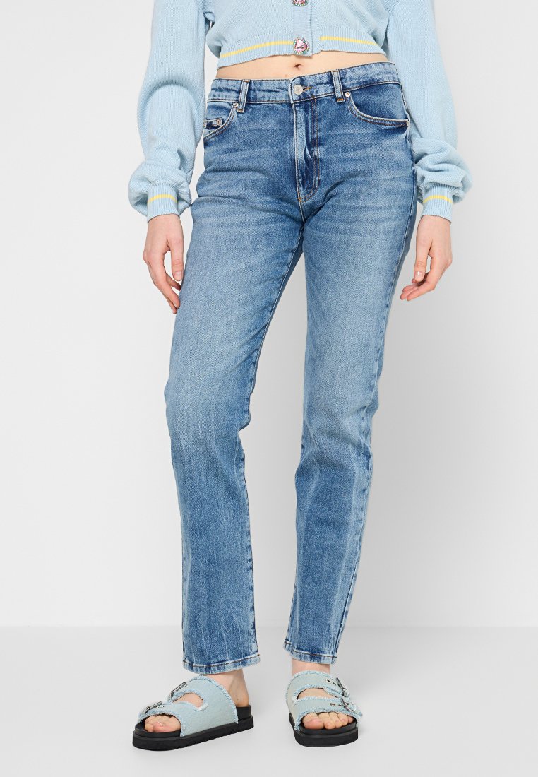 Lichtblauwe denim jeans met een rechte snit, vijf zakken en gestikte naden. Gecombineerd met een lichtblauwe trui en dikke sandalen.