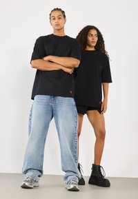 Svarte oversized t-skjorter med rødt hjerte-logo, sammen med lyseblå vide jeans og svarte chunky-helte støvler på to modeller.