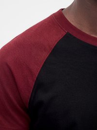 Primo piano di una persona che indossa una maglietta nera con maniche e colletto bordeaux, mostrando la trama del tessuto e i dettagli delle cuciture.