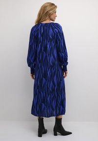 Mekko, jossa on pitkät hihat ja midi-pituus, tummansininen tausta, jossa on sinisiä abstrakteja aalto-kuvioita. Hihansuut on nyöritetty ja kaula-aukko on pyöreä.