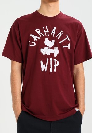 Burgundy cotton t-shirt featuring bold white text reading "Carhartt WIP" with graphics of a bird and a dumbbell. Short sleeves, relaxed fit.