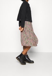 Schwarze Jeansjacke, blumenkleid in Pink mit grünen Akzenten und schwarze Schnürstiefel mit dicker Sohle. Lässiges, geschichtetes Outfit mit ausgeprägten Mustern.