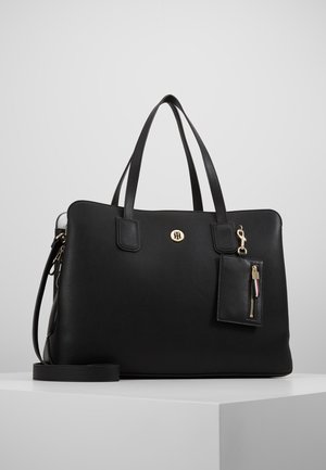 Sac cabas en cuir noir avec double poignée, bandoulière détachable, emblème logo doré, et petite pochette zippée attachée avec fermeture dorée.