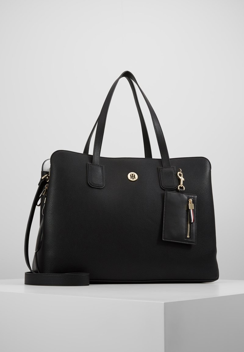 Sac cabas en cuir noir avec double poignée, bandoulière détachable, emblème logo doré, et petite pochette zippée attachée avec fermeture dorée.