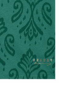 Tejido verde con un patrón damasco texturizado en un tono verde más oscuro, con un logo en rosa dorado que dice "FREDDY training" en la parte inferior.
