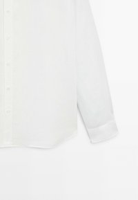 White linen shirt with long sleeves, button-down front, and a semi-structured design. Cuffs feature a smooth texture and rounded hem.