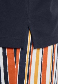 Dunkelblauses Baumwollhemd mit einem gespaltenen Saum, das sich über einen mehrfarbigen gestreiften Stoff in Orange, Gelb, Dunkelblau und Weiß legt.