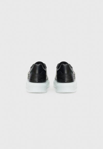 Baskets noires avec un motif reptilien texturé, semelles blanches et détails subtils à l'arrière. Tige en cuir lisse et semelle contrastante.
