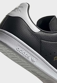 Schwarze Ledersneaker mit weißen Akzenten, strukturiertem Zehenbereich und Gummisohle. Enthält das "adidas"-Logo und Perforationen für Atmungsaktivität.