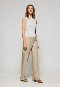 Top blanco sin mangas combinado con pantalones de pierna ancha beige y sandalias de tacón marrones, mostrando texturas suaves y una silueta ajustada.