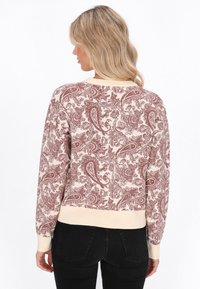 Maglione lavorato a maglia color crema con un motivo paisley bordeaux, dotato di polsini e orlo a costine. Il retro è caratterizzato da una texture intricata.