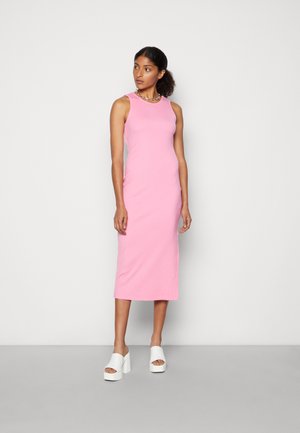 Vestido midi rosa sem mangas, feito de algodão suave, apresentando uma silhueta ajustada. Combinado com sapatos de plataforma brancos de bico aberto.