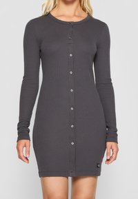 Grå långärmad klänning i ribbad tyg, med knappslutning framtill och en liten logotypapplikation vid fållen.