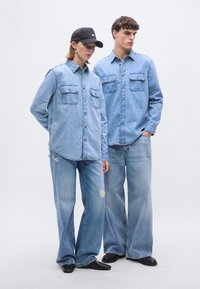 Dva modela nosita svetlo modre denim srajce z dvema sprednjima žepoma, kombinirano z širokimi svetlo modrimi jeans hlačami, pri čemer ima en par obrabljeno podrobnost.