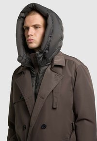 Brown trench coat with a puffer hood, featuring a double-breasted design, dark buttons, and a zippered inner layer. Smooth and textured materials.