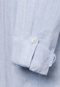 Helles blaues Baumwollhemd mit einem Knopfverschluss an der Manschette und genähten Details, aus einem weichen, strukturierten Stoff mit subtiler gewebter Musterung.