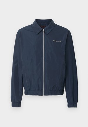 Veste zippée bleu marine Michael Kors avec col, poignets et ourlet élastiques, et logo sur le côté gauche de la poitrine.