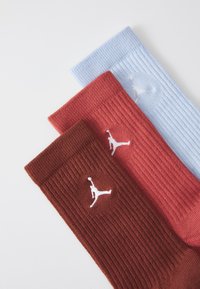Drie paar sokken in blauw, kastanjebruin en roestbruin, met een geribbelde textuur en een wit Jumpman-logo op elk paar.