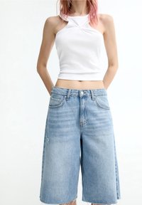 Top corto blanco ajustado con un diseño retorcido en la parte frontal, combinado con culottes de mezclilla azul claro que presentan un dobladillo deshilachado y un estilo clásico de cinco bolsillos.