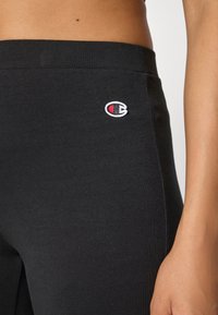 Kvinne iført svarte Champion tights som viser midje- og hofteområdet med logoen på venstre side nær livlinjen.