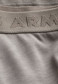 Gros plan d'une ceinture en tissu gris avec des lettres en relief « ARM » sur un matériau doux et tricoté.