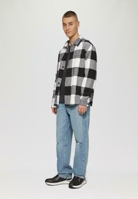 Zwart-wit geblokt flanellen shirt met twee voorzakken, gecombineerd met lichtblauwe gescheurde jeans en zwarte sportschoenen.