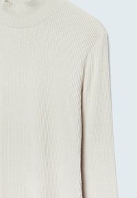 Pull à col roulé beige à côtes avec un tissu texturé, des manches longues et une coupe ajustée.