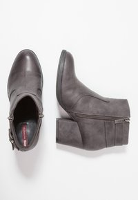 Botas de tobillo grises fabricadas en cuero sintético. Presentan un tacón grueso, cremallera lateral y detalles de costura. Textura suave con un acabado mate.