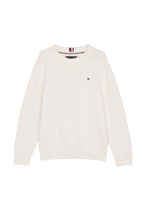 Maglione a maglia off-white con scollo rotondo, abbinato a pantaloni blu navy. Sneakers bianche con accenti di branding discreti. Outfit casual.
