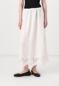 Weißer Leinen-Maxi-Rock mit gerafftem Taillenbund und kunstvollem floralen Cut-out-Design am Saum. Kombiniert mit schwarzen flachen Schuhen.