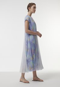 Vestido de color pastel, fluido, con mangas cortas, diseño plisado y superposición translúcida. Presenta suaves patrones en azul, amarillo y verde.