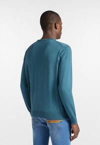 Türkisfarbener Pullover mit Rundhalsausschnitt und langen Ärmeln, mit gerippten Bündchen und Saum. Getragen mit blauen Jeans, die einen lässigen Look zeigen.