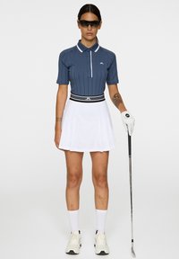 Golfoutfit med en marinblå randig polo med vita detaljer och en vit plisségrej. Vita golfhandskar och sneakers fulländar looken.