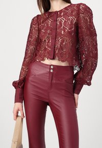 Burgundy spetscroppad topp med blommönster och långa ärmar, tillsammans med figurnära burgundy högmidjade byxor i konstläder.