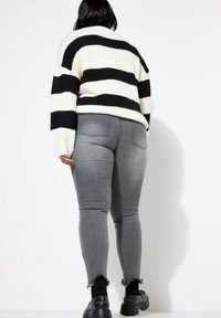 Suéter de rayas blanco y negro, tejido de mezcla de lana. Jeans ajustados grises con bordes deshilachados. Zapatos negros gruesos y calcetas de punto.