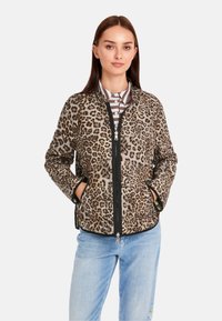 Leoprint-Jacke mit Reißverschluss, seitlichen Taschen, schwarzem Besatz und weichem Material, kombiniert mit einem gestreiften Hemd mit Kragen und Jeans.