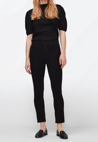 Černé skinny džíny s hladkým povrchem, doplněné černým topem s krátkým rukávem a nařasenými rameny, spárované s černými mokasíny.