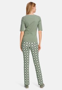 Grünes Kurzarm-Oberteil, kombiniert mit gemusterten, weiten Hosenträgerhosen mit geometrischen Designs in Grün, Schwarz und Weiß, mit einer glatten Oberfläche.