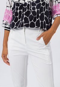 Witte strakke broek met ritszakken, in combinatie met een zwart-wit gebloemde blouse met roze accenten en ballonmouwen.